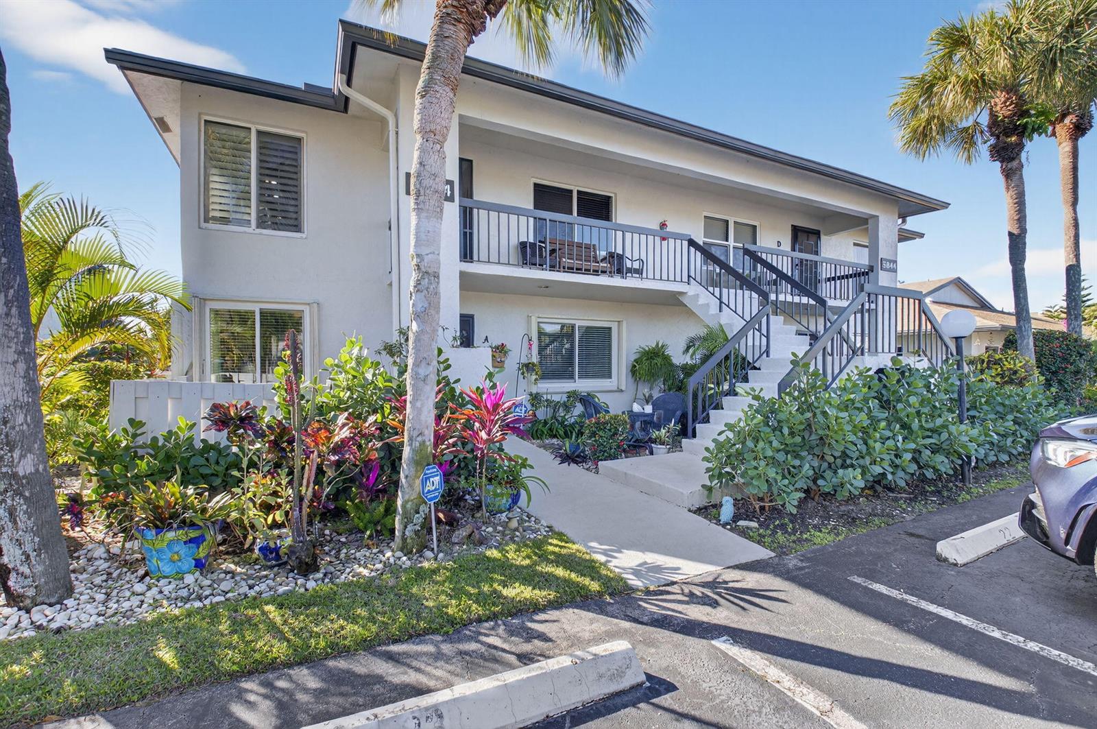 A two-story apartment building with a balcony, exterior staircase, and landscaped front garden — 5844 Areca Palm Ct., Unit B, Delray Beach FL 33484, DELRAY BEACH, FL