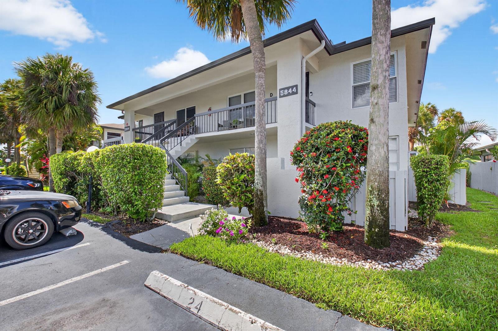 A two-story apartment building features a white exterior, a staircase, and a parking space — 5844 Areca Palm Ct., Unit B, Delray Beach FL 33484, DELRAY BEACH, FL