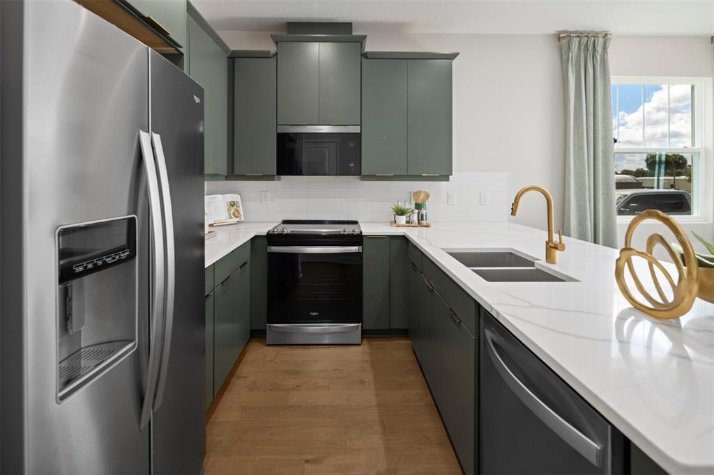 A modern kitchen features dark green cabinets, stainless steel appliances, and a white quartz island — 2820 CAMELLIA FLOWER STREET, APOPKA, FL