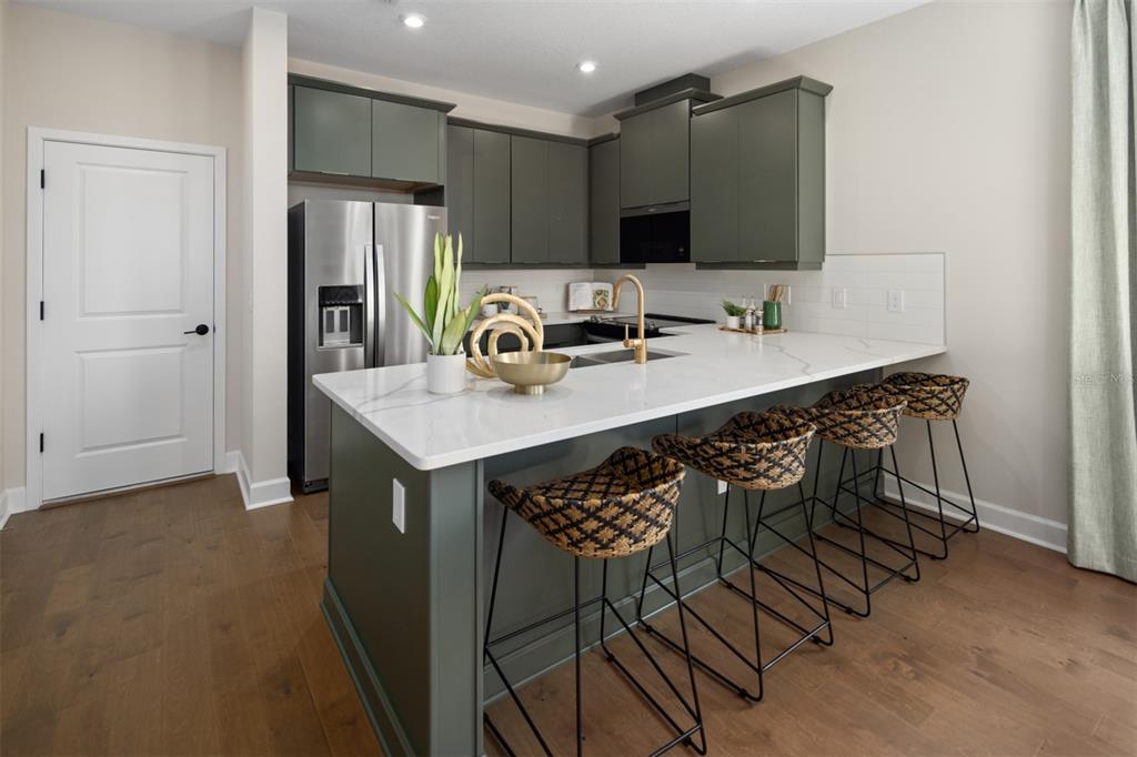 A kitchen features dark green cabinets, a white quartz island, and four woven bar stools — 2820 CAMELLIA FLOWER STREET, APOPKA, FL