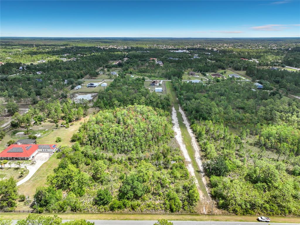 An aerial view shows a large, wooded vacant lot next to a house with solar panels — 00 PADDOCK STREET, ORLANDO, FL