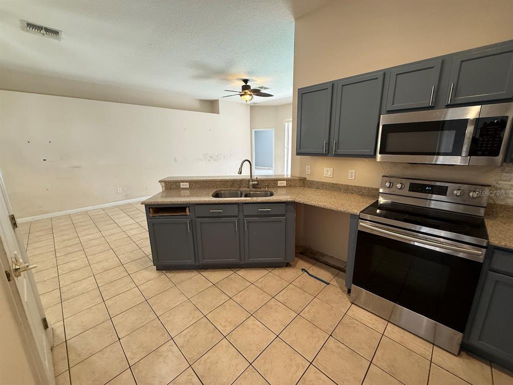 A kitchen with gray cabinets, stainless steel appliances, and tile flooring overlooks an open living area — 3045 MERLOT WAY, CLERMONT, FL