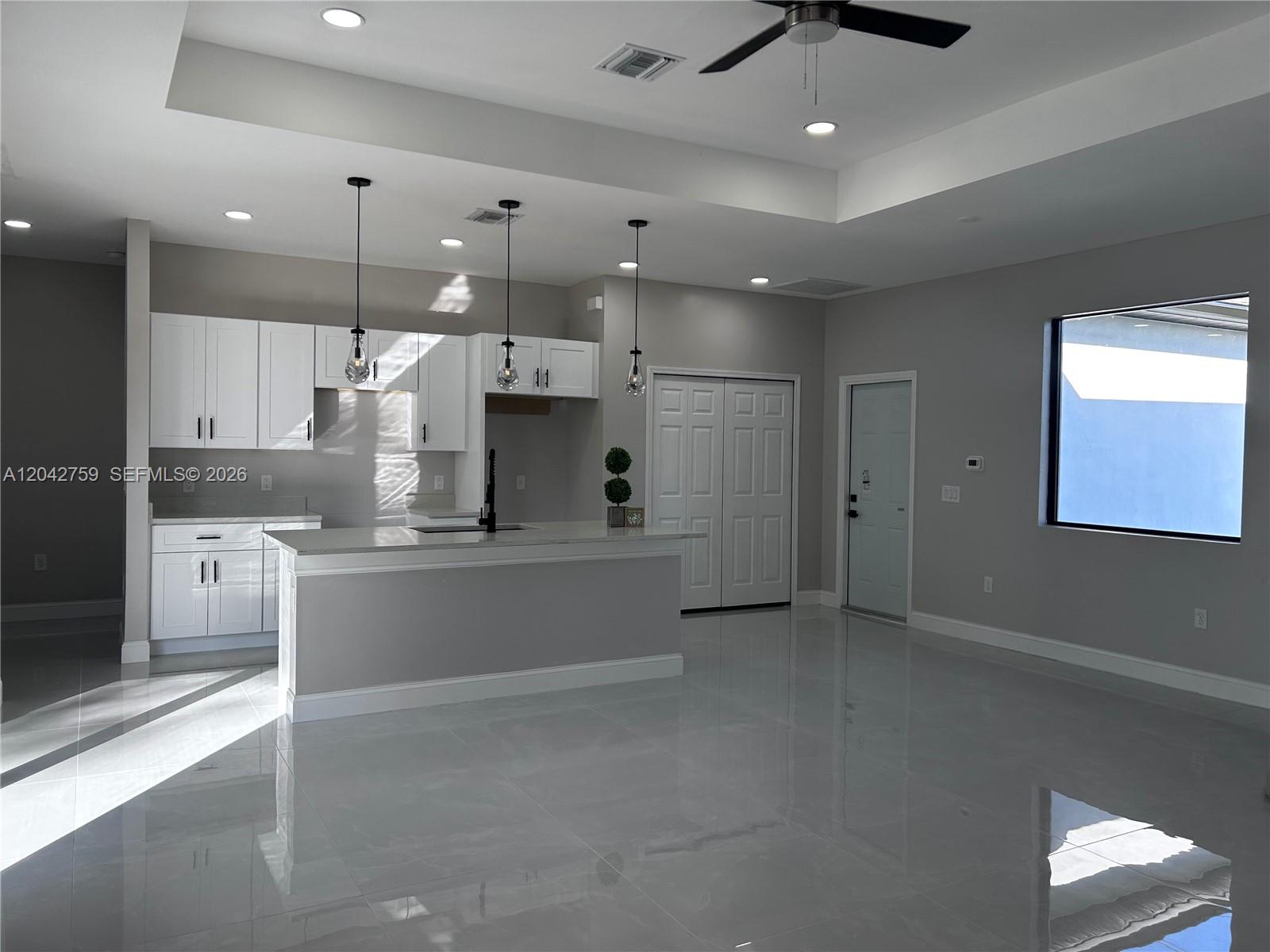 A modern kitchen features white cabinets, a central island, and glossy tile flooring — 1126 Milwaukee Blvd, Lehigh Acres FL 33974, LEHIGH ACRES, FL
