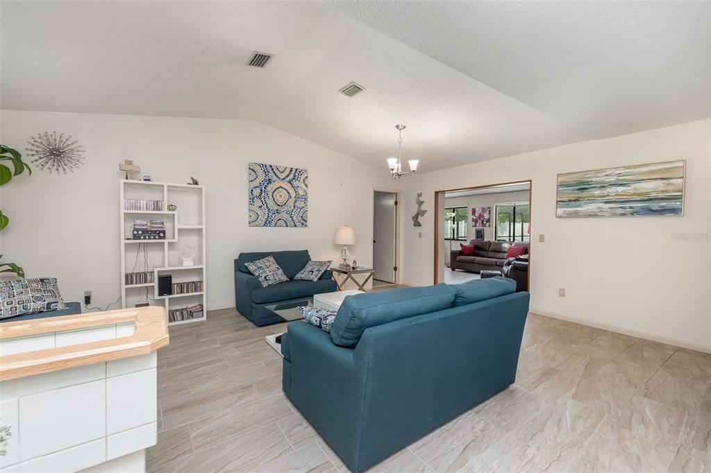 A living room features light tile flooring, blue sofas, a white bookshelf, and vaulted ceilings — 7 PERKINS LANE, PALM COAST, FL