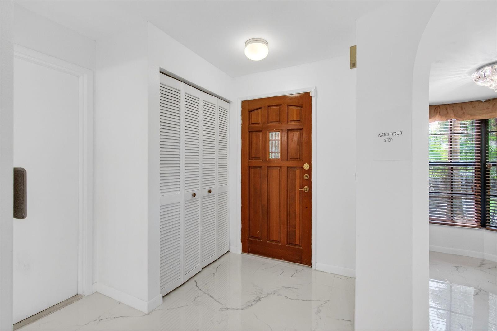 An entryway features white marble-look tile flooring, a wooden front door, and white louvered closets — 7865 La Mirada Drive, Boca Raton FL 33433, BOCA RATON, FL