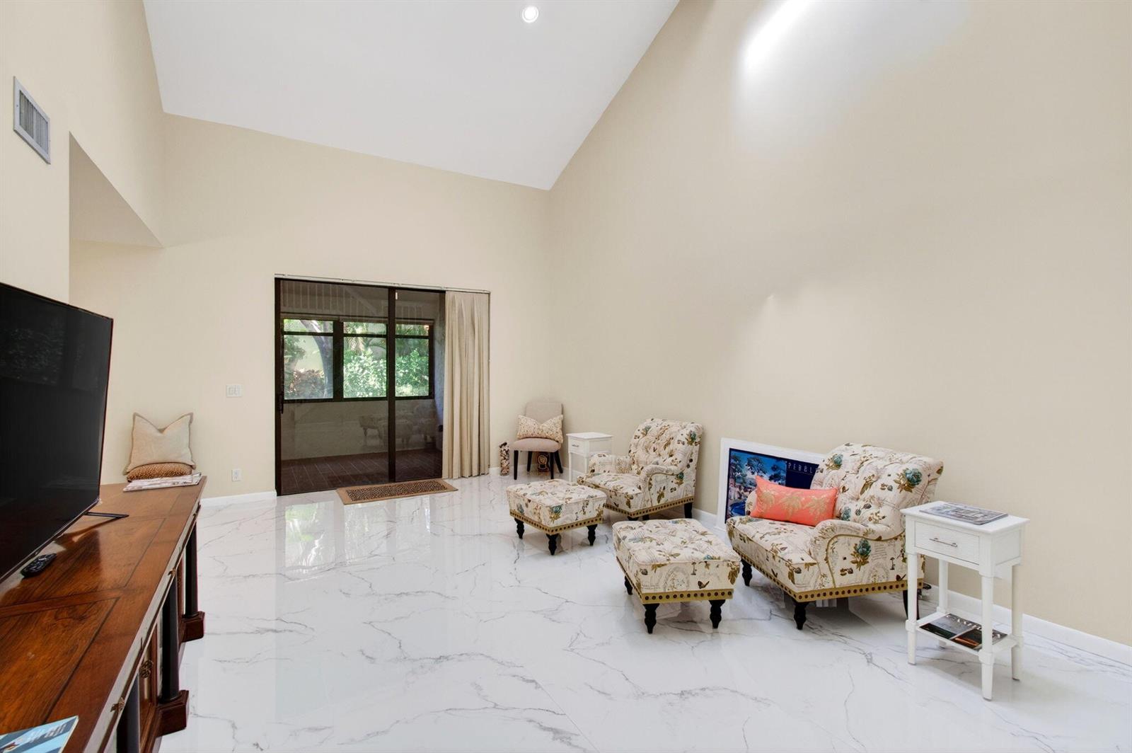 A living room with vaulted ceilings, white marble-look tile flooring, and floral armchairs — 7865 La Mirada Drive, Boca Raton FL 33433, BOCA RATON, FL