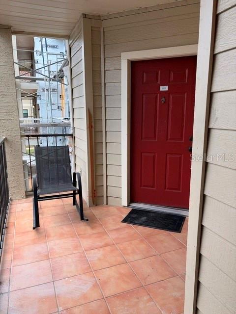 A red door opens onto a tiled balcony with a metal chair and exterior siding — 3036 PARKWAY BOULEVARD UNIT 205, KISSIMMEE, FL