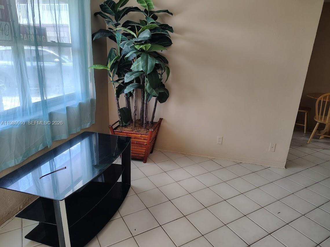 A room with white tiled floors, a black glass TV stand, and a large potted plant — 1816 Mckinley St # 2, Hollywood FL 33020, HOLLYWOOD, FL
