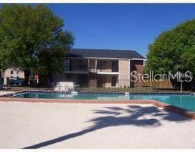 A swimming pool sits in front of a two-story apartment building with trees nearby — 4015 MY LADY LANE UNIT 6, LAND O LAKES, FL