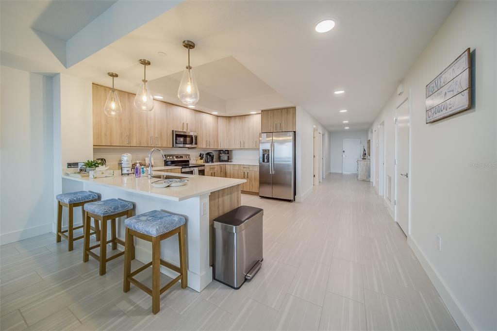 A modern kitchen features light wood cabinets, stainless steel appliances, and a white breakfast bar — 415 ISLAND WAY UNIT 505, CLEARWATER, FL