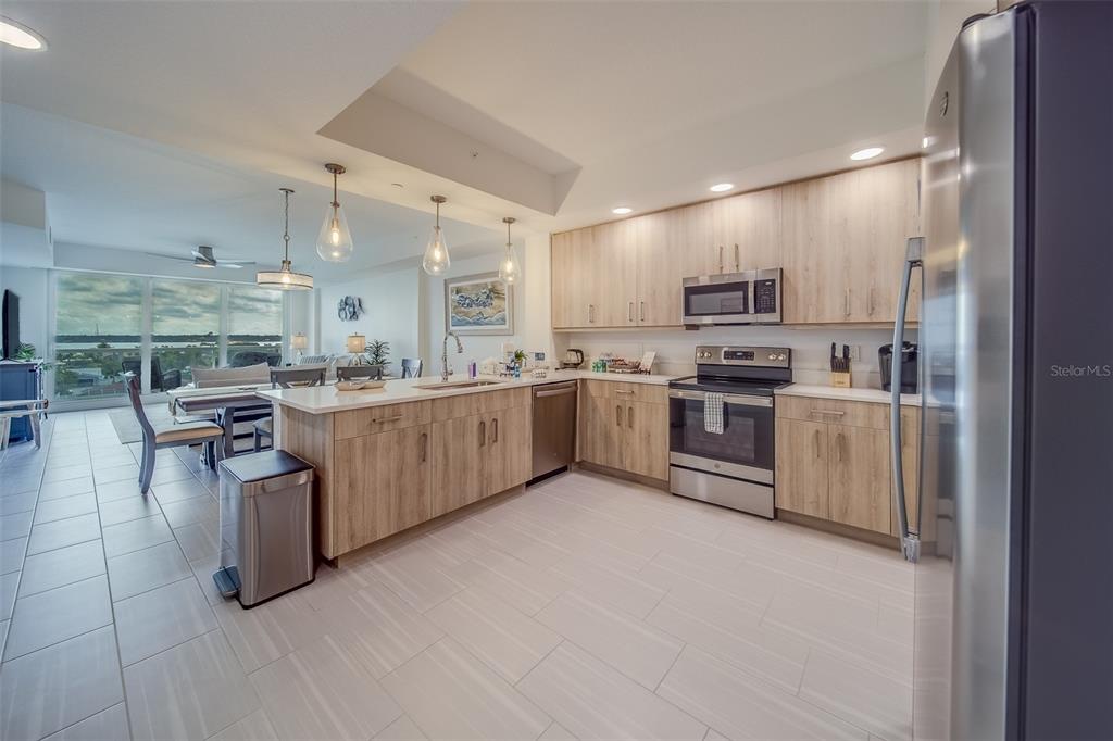 A modern kitchen features light wood cabinets, stainless steel appliances, and an island with seating — 415 ISLAND WAY UNIT 505, CLEARWATER, FL
