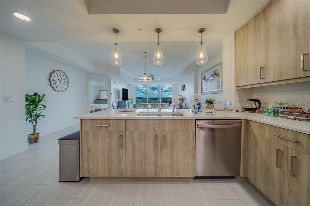 A modern kitchen features light wood cabinetry, white countertops, stainless steel appliances, and pendant lighting — 415 ISLAND WAY UNIT 505, CLEARWATER, FL