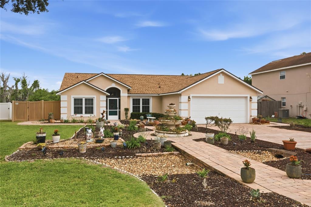 A single-story house with a tan exterior, a two-car garage, and a landscaped front yard — 204 GREENWICH STREET, DAVENPORT, FL