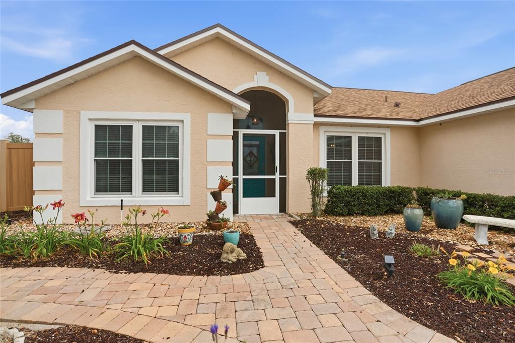 A tan single-story house features a paved walkway, a screened front door, and landscaped beds — 204 GREENWICH STREET, DAVENPORT, FL