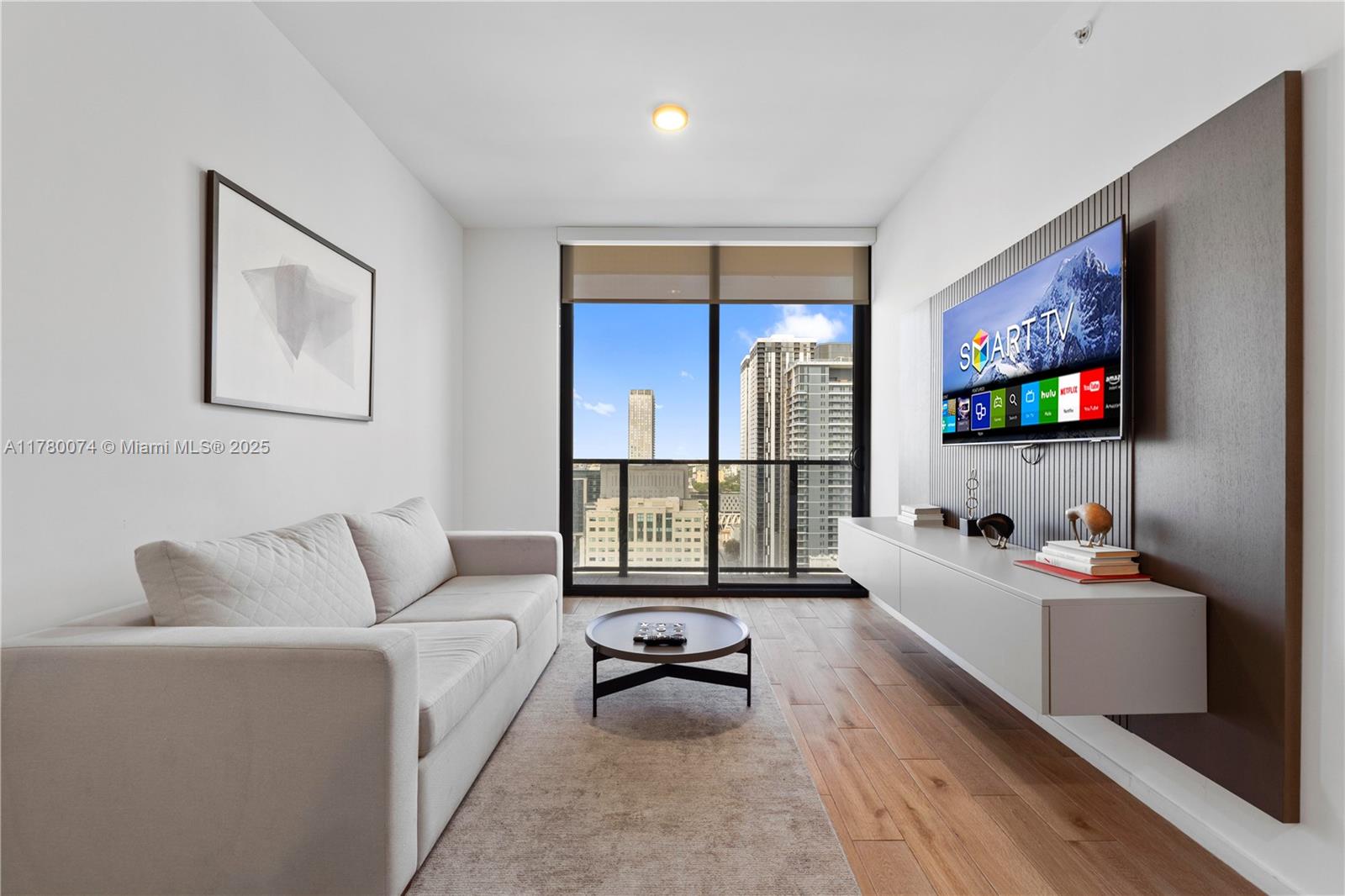 A modern living room features a light-colored sofa, a wall-mounted television, and a balcony view — 398 NE 5th St # 2119, Miami FL 33132, MIAMI, FL