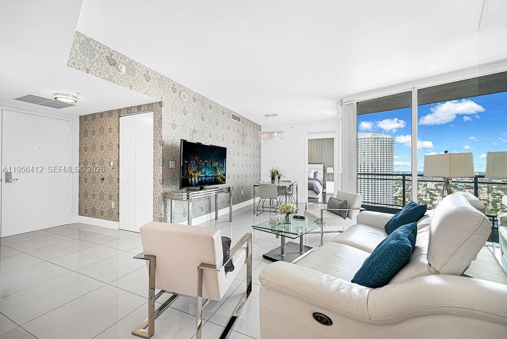 A modern living room features white tile floors, patterned wallpaper, and floor-to-ceiling windows with city views — 92 SW 3rd St # 4806, Miami FL 33130, MIAMI, FL