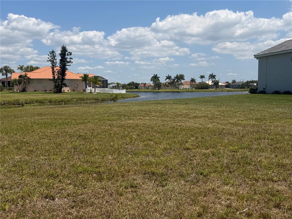 A grassy vacant lot overlooks a canal with houses and palm trees in the distance — 16201 CAYMAN LANE, PUNTA GORDA, FL
