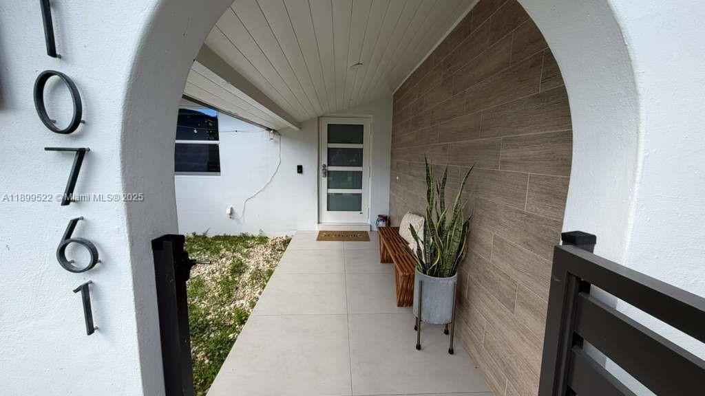 A covered entryway features a wood-look tiled wall, a modern front door, and a bench — 10761 SW 165th St, Miami FL 33157, MIAMI, FL