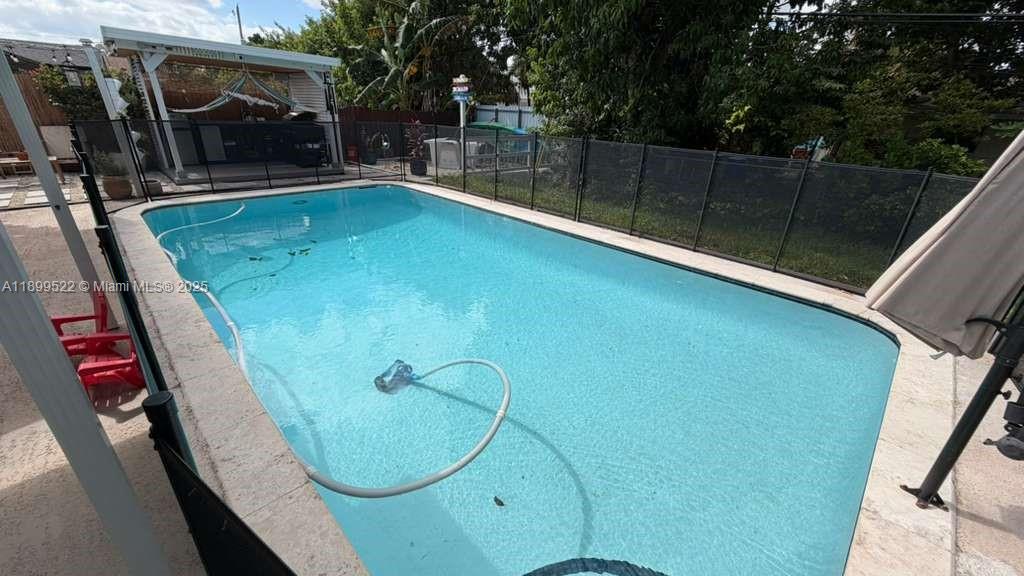 A rectangular swimming pool with a safety fence and a covered patio area nearby — 10761 SW 165th St, Miami FL 33157, MIAMI, FL