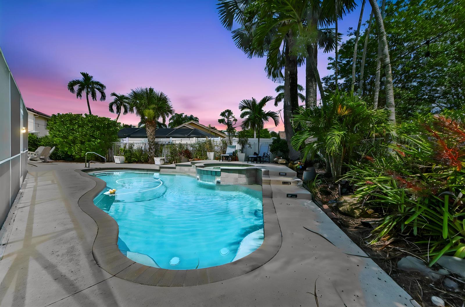 A backyard swimming pool with an attached spa is surrounded by palm trees at sunset — 7461 Anadale Circle, Lake Worth FL 33467, LAKE WORTH, FL