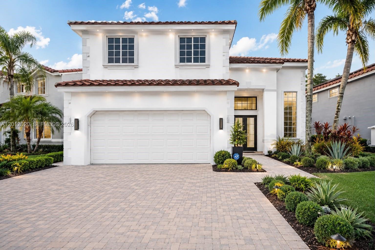 A two-story white stucco house features a two-car garage, tile roof, and landscaped front yard — 303 Bridgeton Rd, Weston FL 33326, WESTON, FL
