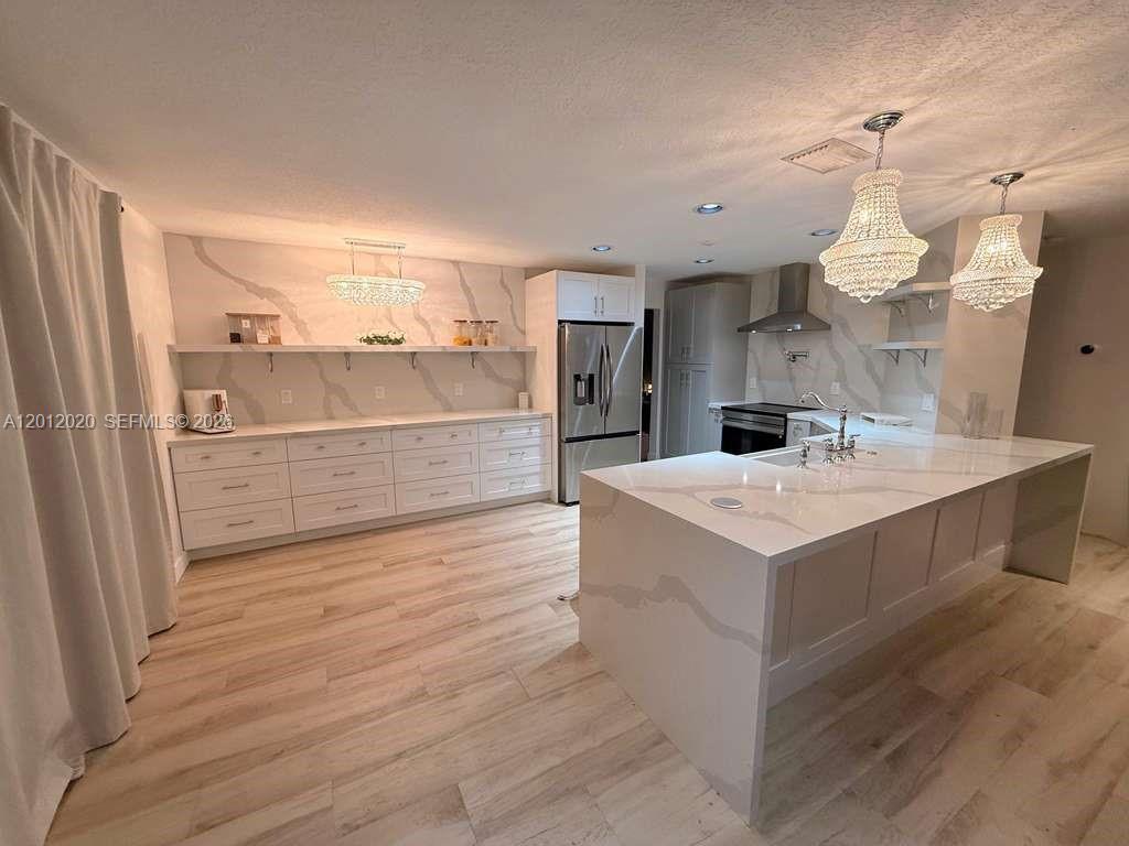 A modern kitchen features white cabinetry, marble-patterned countertops, a large island, and crystal chandeliers — 303 Bridgeton Rd, Weston FL 33326, WESTON, FL