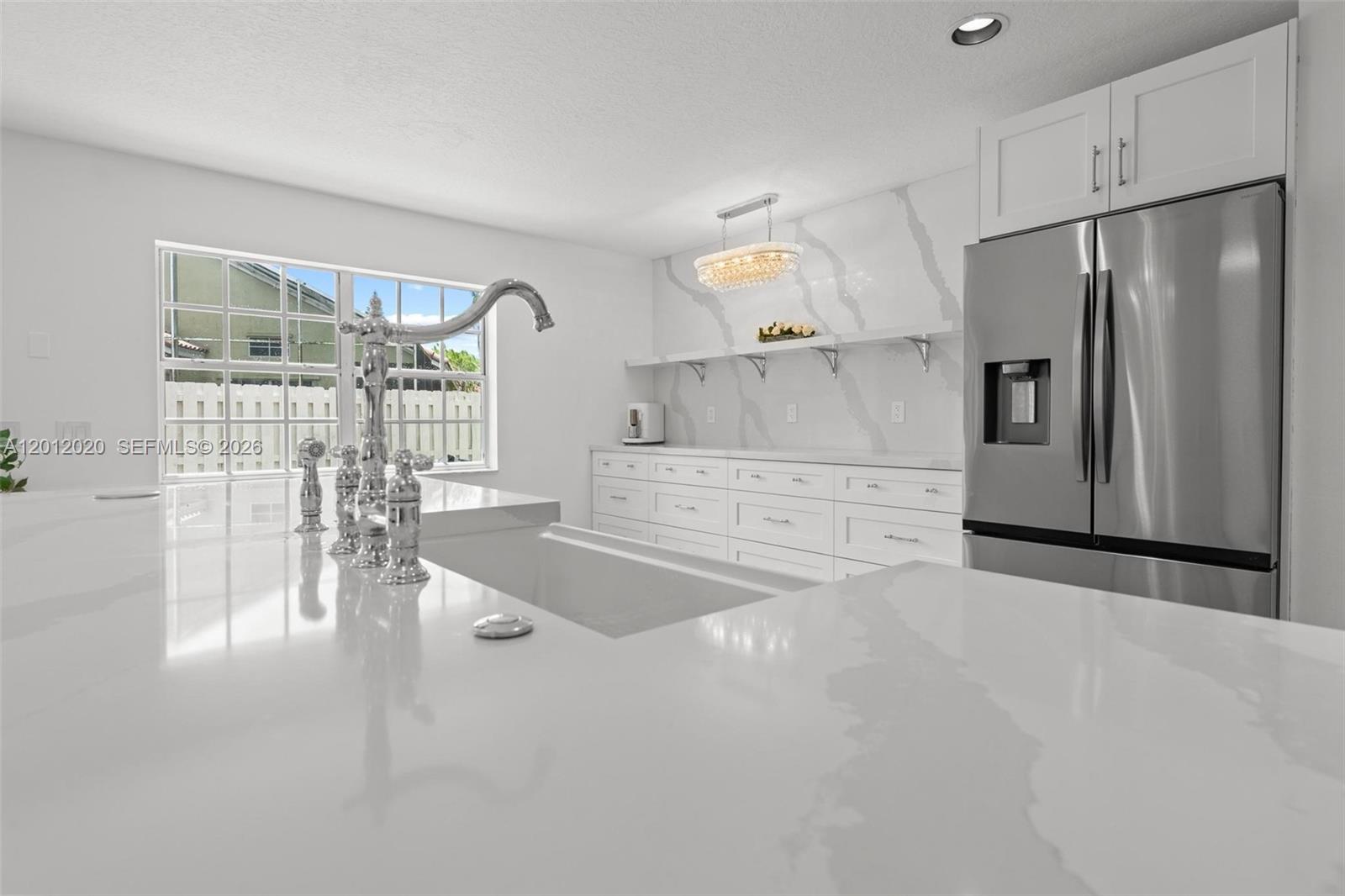 A modern white kitchen features a large island, marble-style backsplash, and stainless steel refrigerator — 303 Bridgeton Rd, Weston FL 33326, WESTON, FL