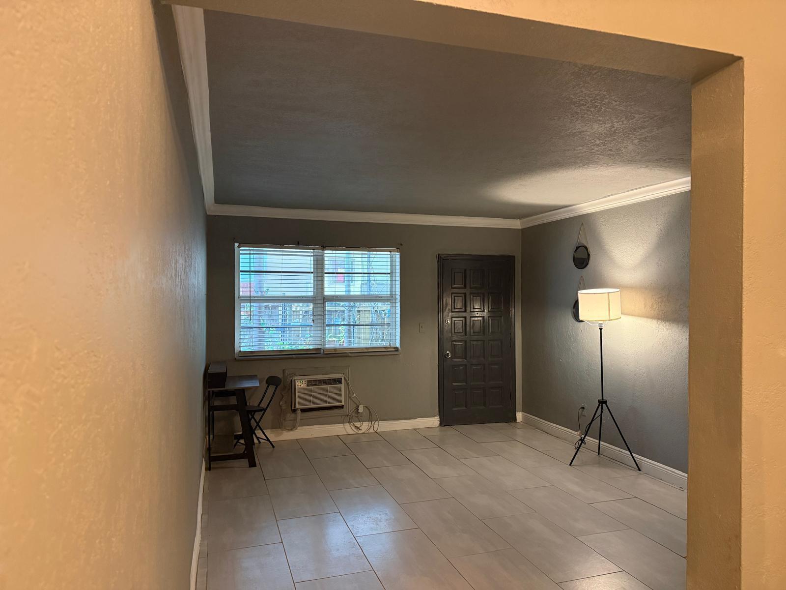 A room with gray walls, tile flooring, a window with blinds, and a tripod floor lamp — MIAMI BEACH, FL