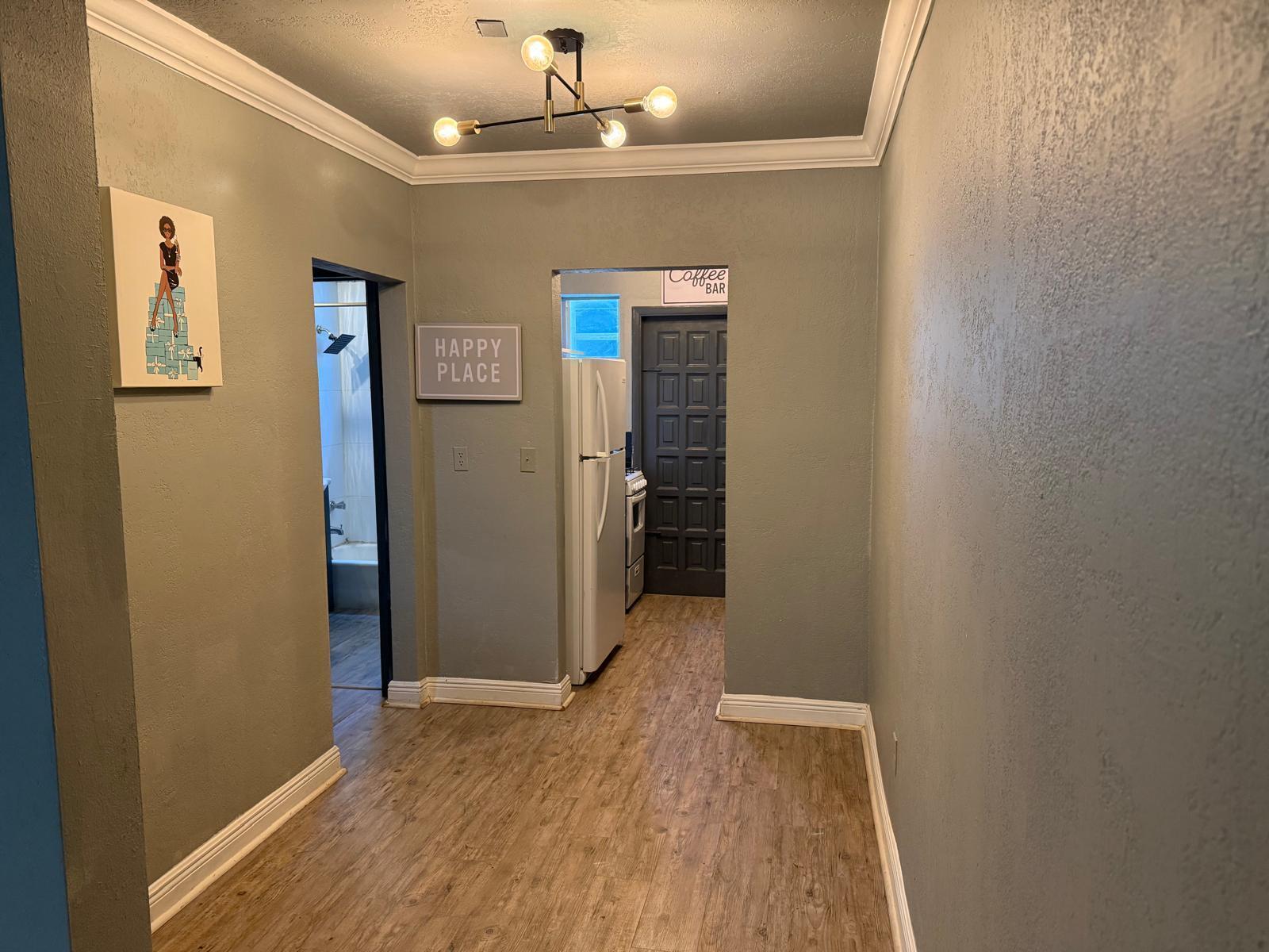 A hallway with light wood flooring, gray walls, and a modern light fixture leads to rooms — MIAMI BEACH, FL