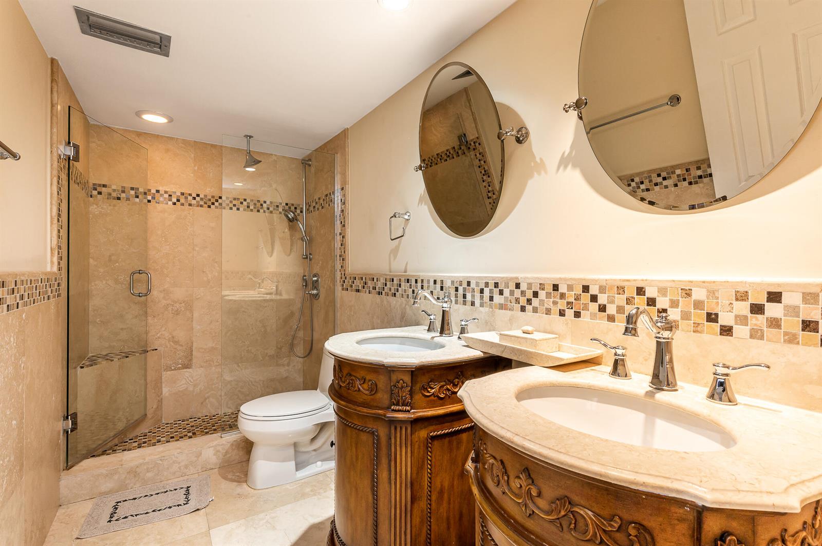 A bathroom features two ornate wooden vanities, a glass-enclosed shower, and beige stone tile walls — 2800 N Ocean Drive # 2b, Singer Island FL 33404, SINGER ISLAND, FL