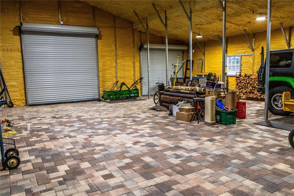 A spacious garage with a paver floor, yellow spray-foam insulation, and two roll-up doors — 24091 RICHBARN ROAD, BROOKSVILLE, FL