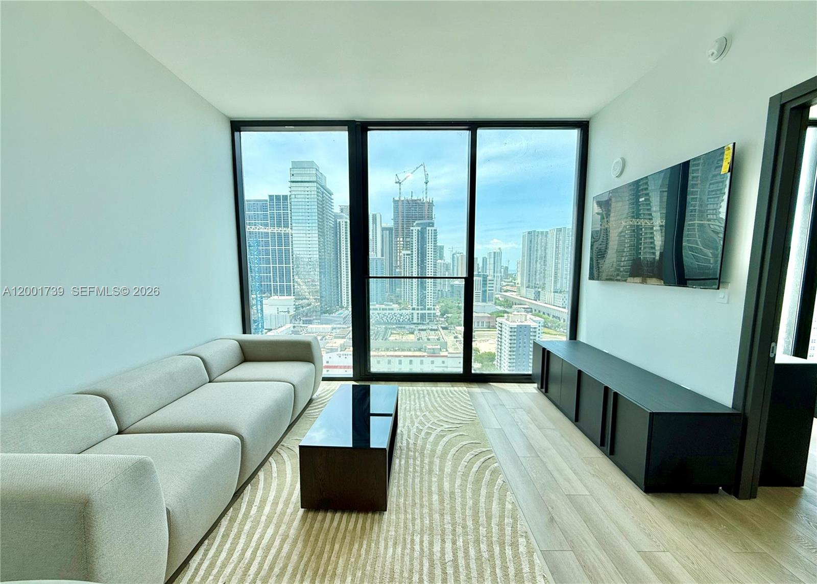 A modern living room features a light-colored sofa, coffee table, and floor-to-ceiling city views — 20 NE 11th St # 2809, Miami FL 33132, MIAMI, FL