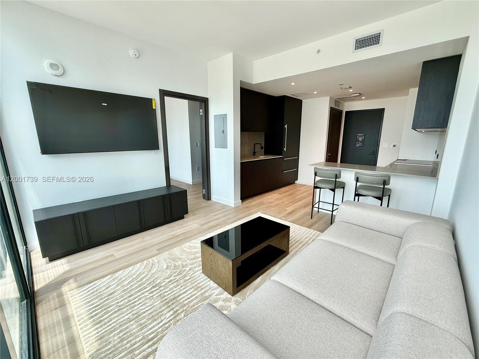 A modern living room features a wall-mounted television, a sofa, and an open kitchen area — 20 NE 11th St # 2809, Miami FL 33132, MIAMI, FL