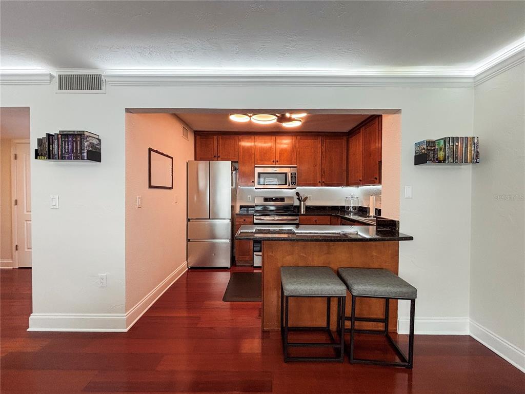A kitchen with wood cabinets, stainless steel appliances, and a breakfast bar with two stools — 210 5TH AVENUE S UNIT 209, ST PETERSBURG, FL