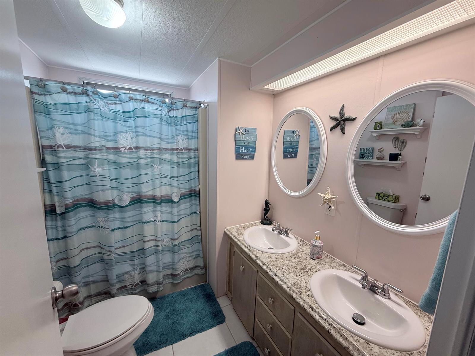 A bathroom with a double vanity, granite countertop, two oval mirrors, and a coastal-themed shower curtain — 225 W 2nd Court, Key Largo FL 33037, KEY LARGO, FL