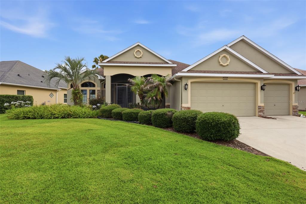 A single-story house with a beige stucco exterior, a three-car garage, and a manicured lawn — 7879 CROSSWINDS WAY, MOUNT DORA, FL