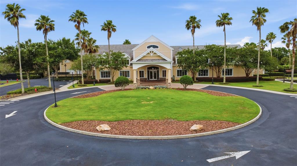 A beige building with a gabled entrance sits behind a circular driveway and lawn — 7879 CROSSWINDS WAY, MOUNT DORA, FL