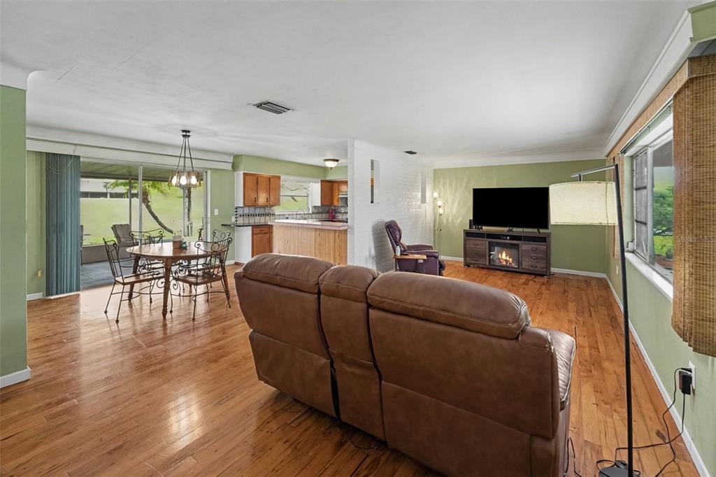 A living room and dining area with hardwood floors, green walls, and a brick fireplace — 6026 44TH AVENUE N, KENNETH CITY, FL