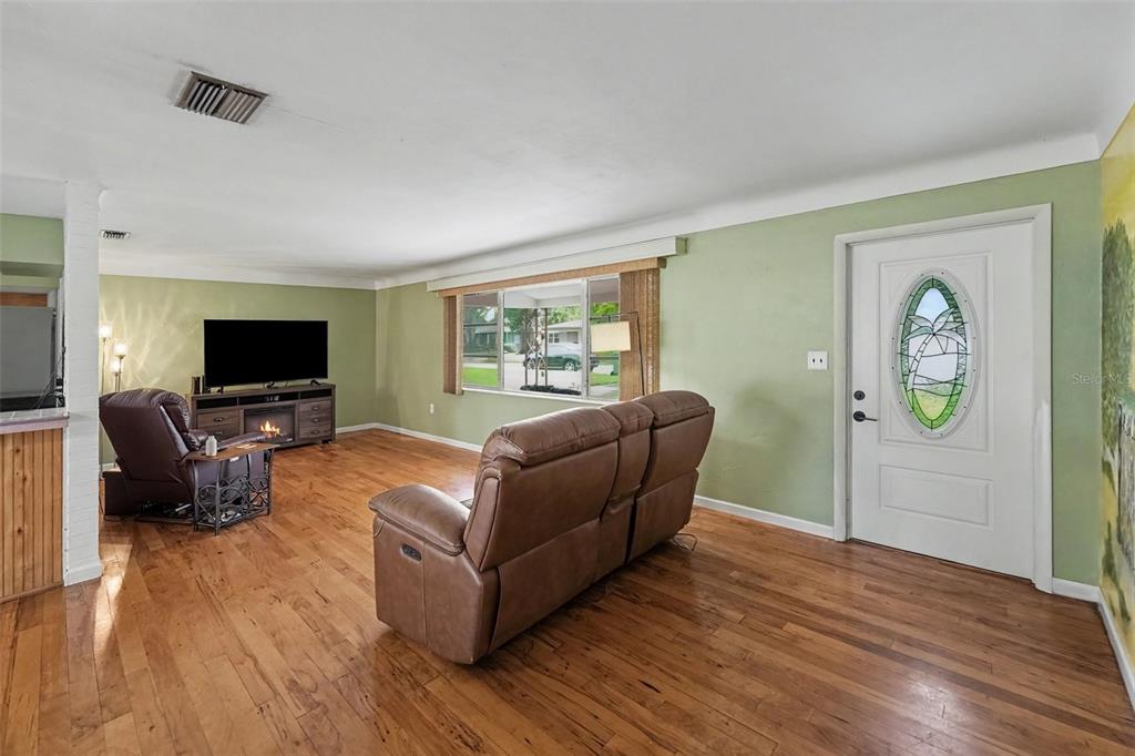 A living room with light green walls, hardwood floors, a brown sofa, and a front door — 6026 44TH AVENUE N, KENNETH CITY, FL