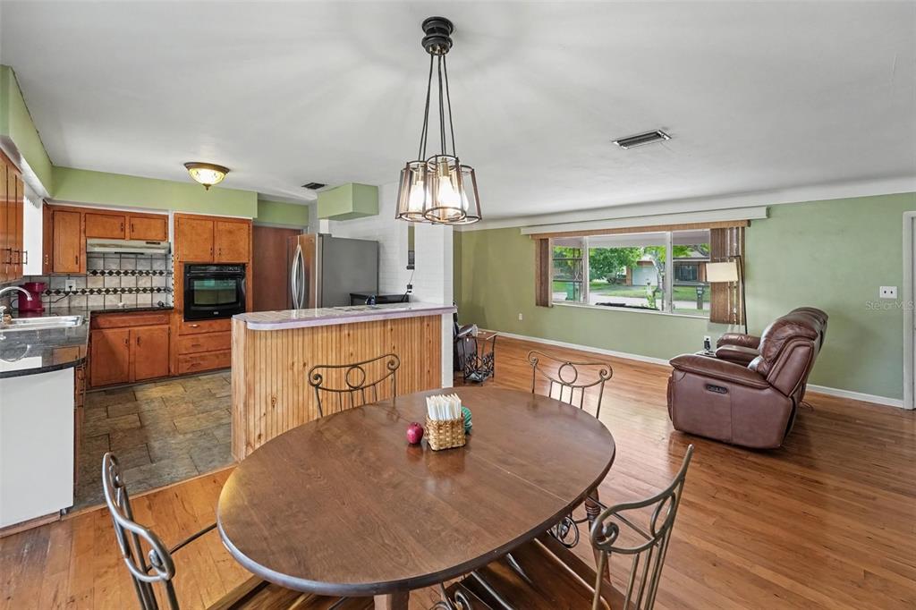 A dining area with a wooden table and chairs opens to a kitchen and living room — 6026 44TH AVENUE N, KENNETH CITY, FL