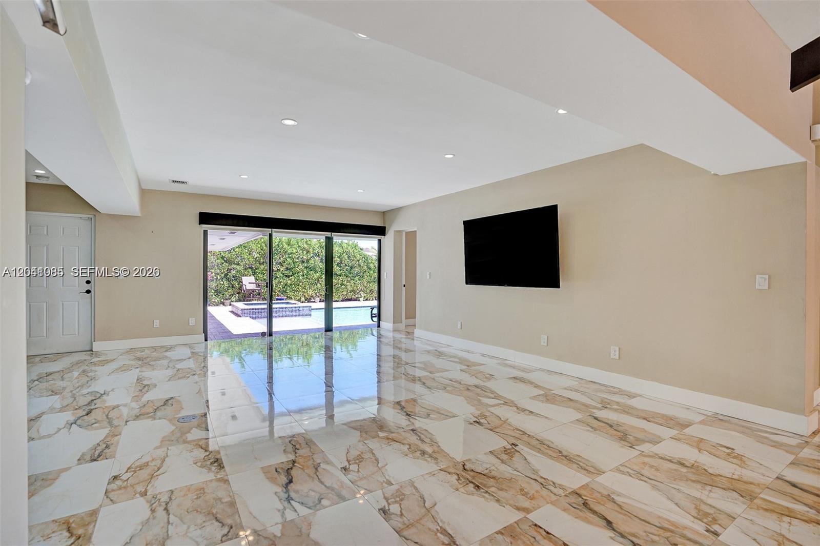 A living room with marble tile flooring, a wall-mounted television, and sliding glass doors — 2255 NE 120th St, North Miami FL 33181, NORTH MIAMI, FL