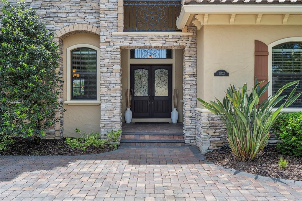 The exterior of a house features a stone facade, double front doors, and a paver driveway — 11753 VINCI DRIVE, WINDERMERE, FL
