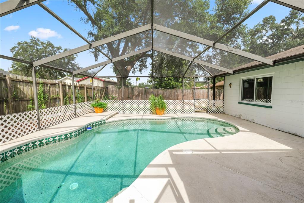 A screened-in swimming pool with a concrete deck sits in a backyard with wooden fencing — 4820 PRESIDENTIAL STREET, SEFFNER, FL