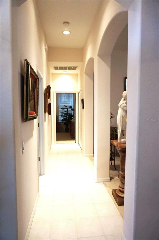A hallway with white tile flooring leads to a doorway with a view of a plant — 11752 WAYSIDE WILLOW COURT, HUDSON, FL