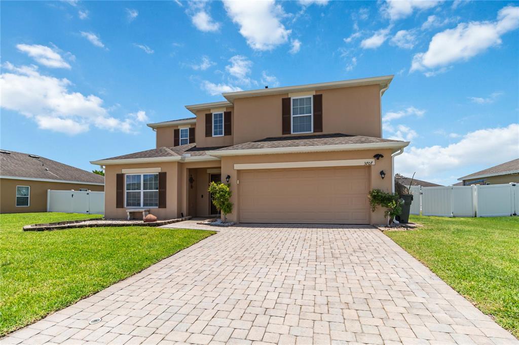 A two-story tan house with a paved driveway, a two-car garage, and a white fence — 3707 BRAMBLY AVENUE, ST CLOUD, FL