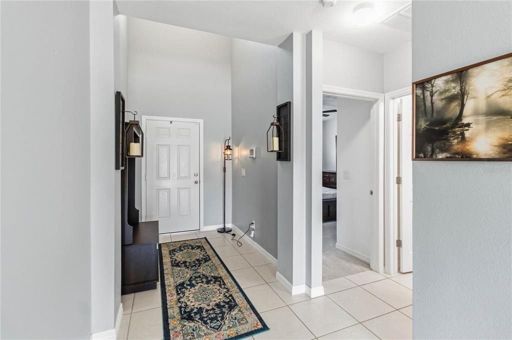 A tiled entryway features a white front door, a runner rug, and wall-mounted lantern sconces — 3707 BRAMBLY AVENUE, ST CLOUD, FL