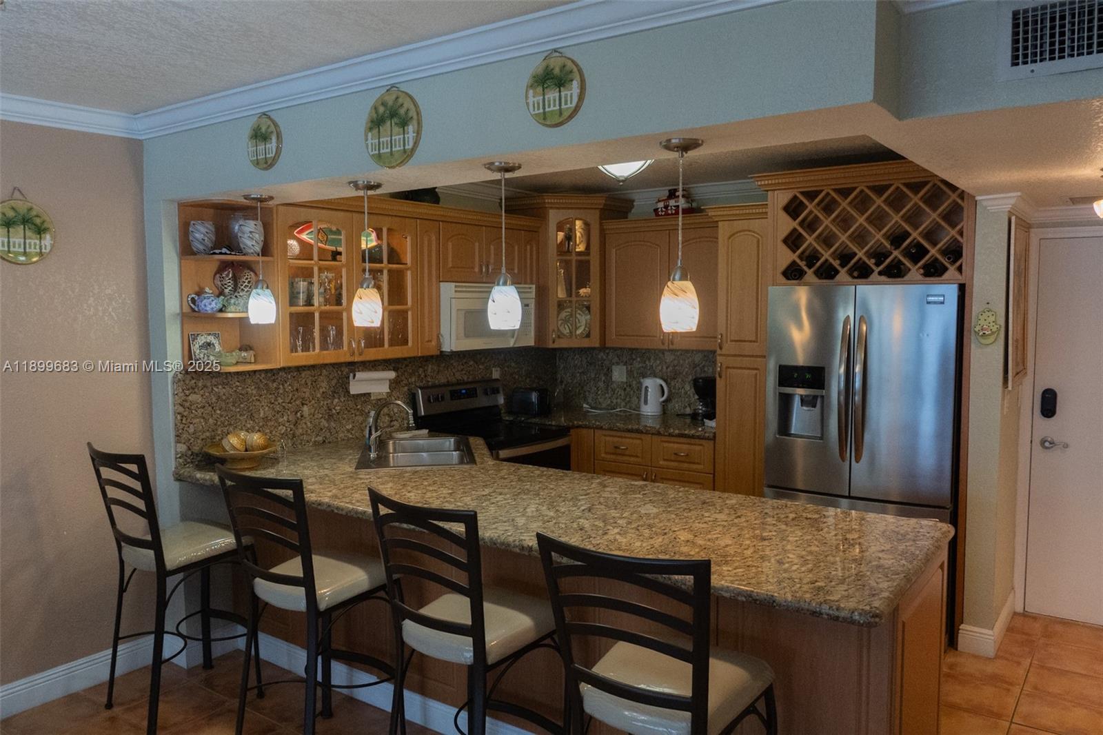A kitchen features light wood cabinets, granite countertops, stainless steel appliances, and four bar stools — 3725 S Ocean Dr # 1021, Hollywood FL 33019, HOLLYWOOD, FL