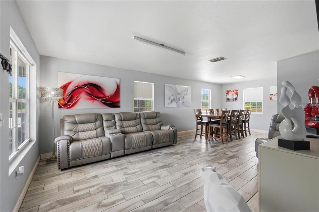 A living and dining room with grey wood-look tile flooring and a grey reclining sofa — 14445 COMMONWEALTH AVENUE N, POLK CITY, FL