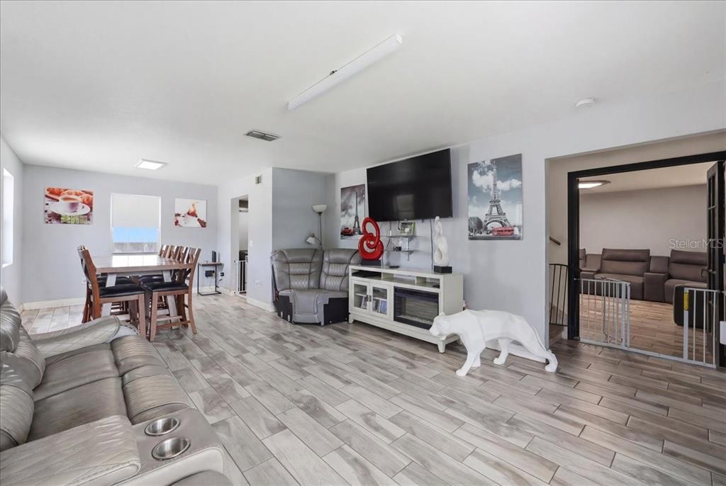 A living room with light wood-look tile flooring, a television, and a dining area — 14445 COMMONWEALTH AVENUE N, POLK CITY, FL