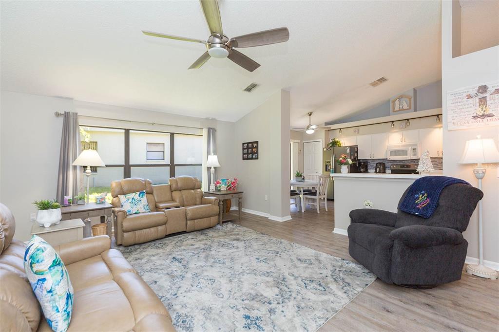 A living room with tan leather seating, a patterned area rug, and an open kitchen — 11321 COPLEY COURT, SPRING HILL, FL